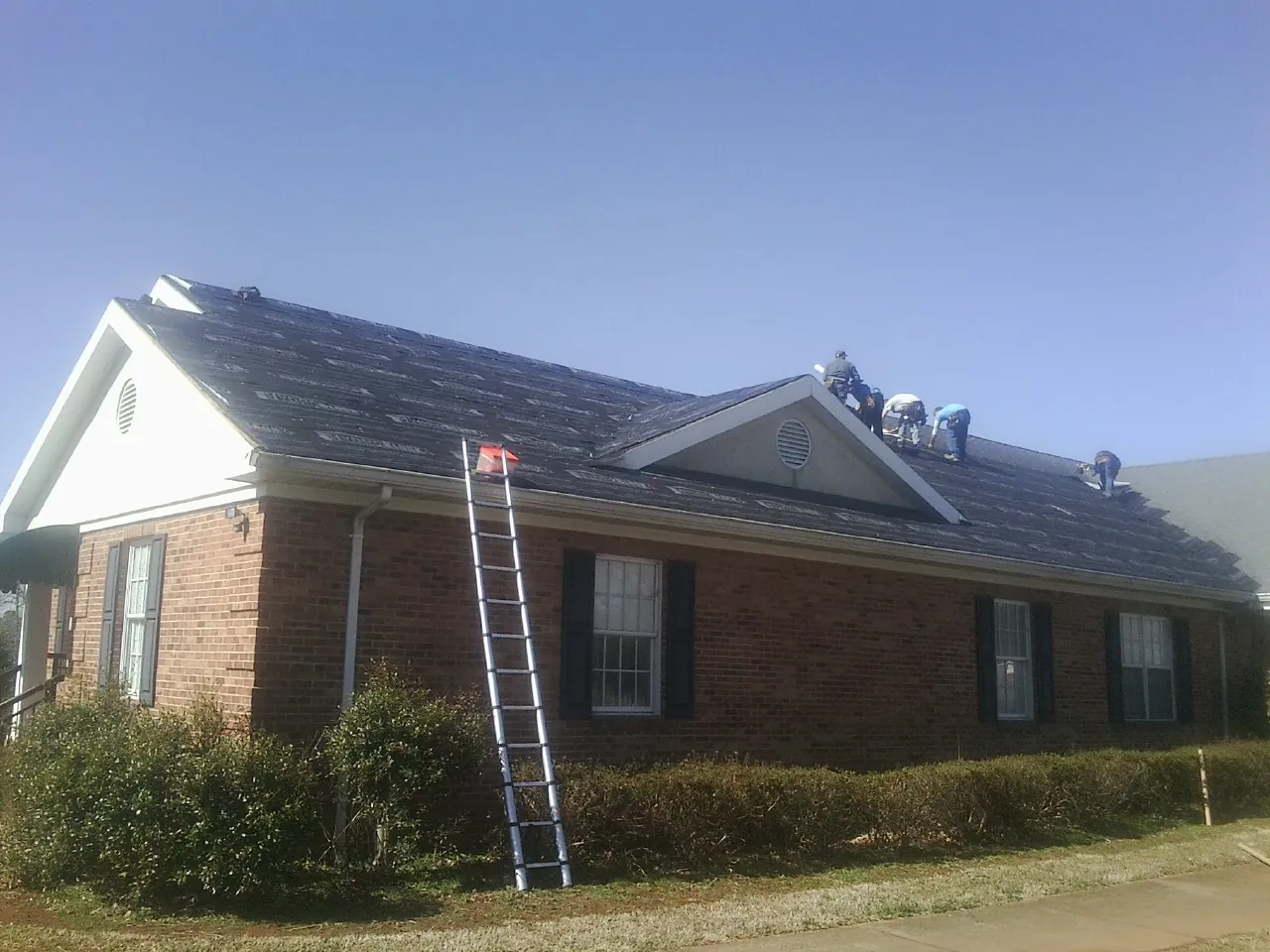 Crew tearing shingles off a brick ranch roof with a ladder set — Metal Roof Repair work by our crew in Hunter