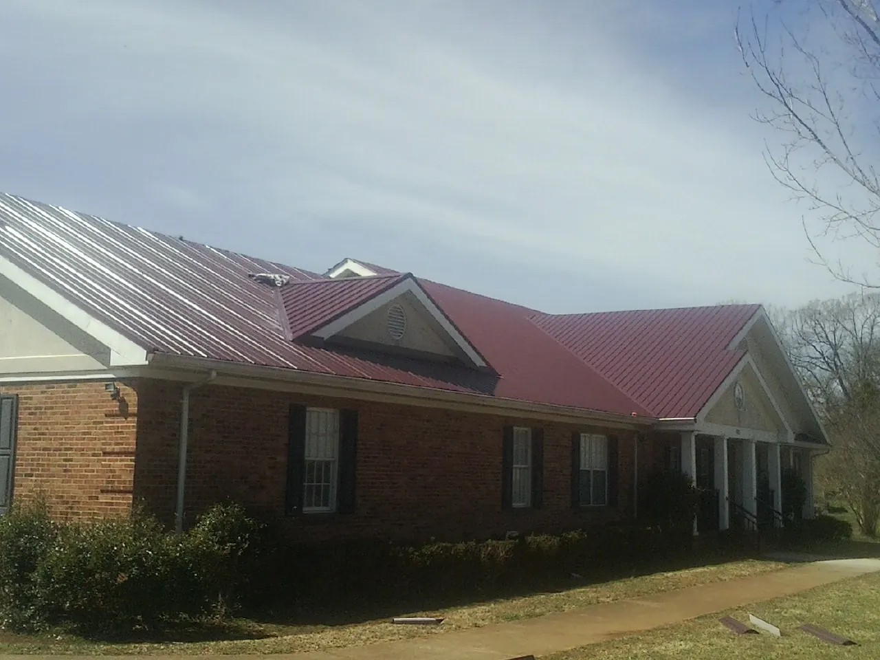Red metal roof with gabled entries on a long brick building, from a Hail Damage Roof Repair job in Hunter