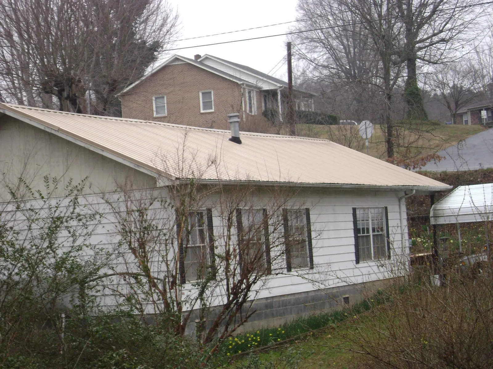 Tan metal roof on a white sided house set into a hillside — Commercial Roofing by Roofing Brothers in Hunter
